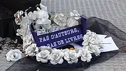 La couronne mortuaire en papier est accompagnée d'un message écrit en blanc sur fond bleu : "Pas d'auteurs, pas de livres."