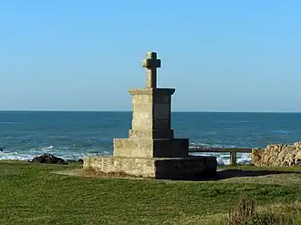 Vue d’une croix en pierre avec la mer en arrière-plan.