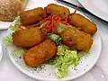 Dans une assiette blanche, six croquettes reposent sur un lit de salade que décore en son centre un peu de carottes râpées.