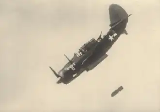 Helldiver SB2C-1 effectuant un bombardement en piqué (1943). On y voit les trappes de soute ouvertes et plus bas la bombe.