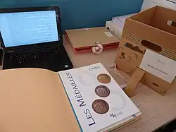 Documents d'archives du CNRS : les dossiers d'archives, un document en cours d'analyse et un ordinateur pour saisir les résultats.