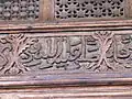 Détail d'une inscription arabe en style naskhi. Elle est sculptée en relief sur la traverse située au-dessous du tympan de la grande porte de la salle de prière.