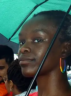 Photographie d'une femme noire souriante aux cheveux afros courts sous un parapluie