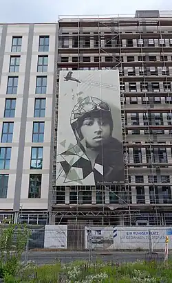 Photographie d'une façade d'immeuble sur laquelle est déployée une bannière représentant Bessie Coleman.