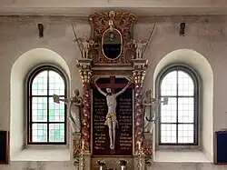 Intérieur médiéval sacré, croix centrale sculptée, lumière tamisée, tons terreux et or.