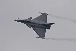Photo d'un Rafale en train de tourner, ce qui fait qu'on voit son dessus. Des trainées de condensation s'échappent des deux bouts d'ailes, donnant une impression de vitesse.