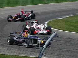 Photo d'une monoplace blanche en piste, entourée d'une monoplace bleue et d'une monoplace rouge et bleue