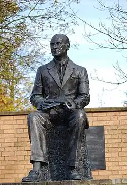 statue représentant un homme assez âgé, en costume, assis, avec une maquette de Comet dans les mains.