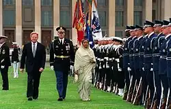 Une femme, accompagnée de deux hommes, dont un militaire, inspecte des militaires en rang.