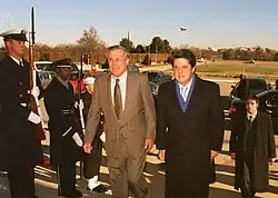 Photo d'hommes en costume avançant le long d'hommes en uniforme portant des fusils