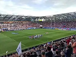 Depuis les tribunes, photo de l'équipe de Grenoble se dirigeant vers les vestiaires. Il fait beau.
