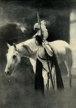 Une femme costumée caresse un cheval blanc.