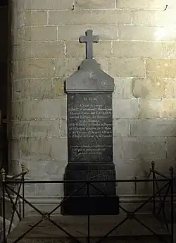 Pierre tombale sombre entourée d'une rembarde adossée à une maçonnerie.