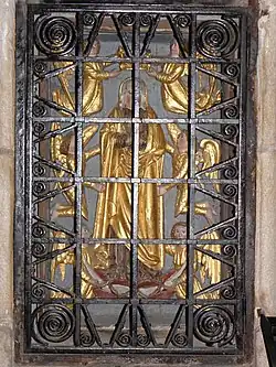 Photographie d'un bas-relief en partie doré derrière une grille.