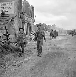 photo présentant des soldats anglais marchant sur une route au bord des ruines d'un village
