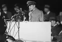MacArthur en uniforme discoure depuis une estrade avec de nombreux micros.