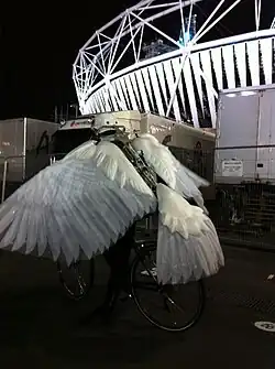 photo d’un costume de colombe ou de pigeon, articulé, composé de deux grandes ailes de plumes blanches réalisées en tissu et d’une queue assortie ; le costume est destiné à être porté par un cycliste