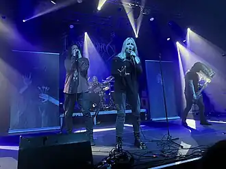 Quatre membres d'un groupe de rock, comprenant trois hommes et une femme, jouant sur scène