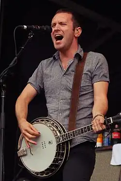 Homme caucasien devant un micro tenant un banjo.