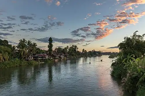 Habitations et pirogues sur la berge de Don Det, au lever du soleil avec des nuages roses, vus depuis le pont de Don Khon.