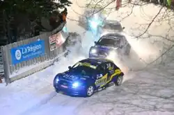 Voitures de course beues, vue de trois-quart avant prenant un virage à droite sur la neige.