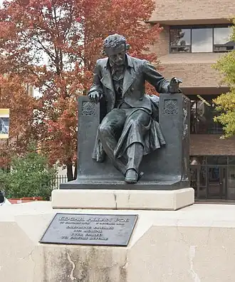 Statue d'un homme assis sur une chaise posée sur un socle de pierre au milieu d'un parc