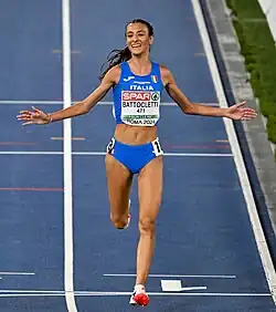 Nadia Battocletti, maillot bleu de l'Italie, écarte les bras en franchissant la ligne d'arrivée.