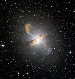 Photographie d'une galaxie, une source lumineuse au centre, formant un anneau et perpendiculairement des lobes moins lumineux.