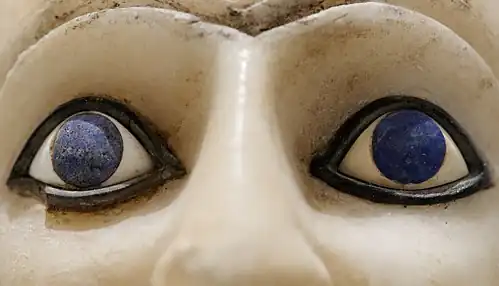 Gros plan des yeux en coquillage, iris en lapis-lazuli, soulignés d'un trait de bitume.