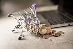 Près d’un ordinateur portable, un panier d’achats sur roues miniature est renversé et déverse des sous.