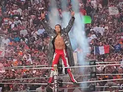 Photo d'un catcheur portant une longue veste saluant la foule en montant sur la deuxième corde.