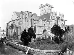 L'église vue du sud-ouest en 1879, figurant la façade sud occupée par un cimetière et des ifs, côté occupé désormais par un parking