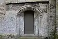 Petite porte basse en plein cintre surbaissé à côté du clocher.