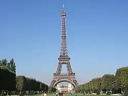 La tour Eiffel devant un ciel bleu et entouré d'arbres.