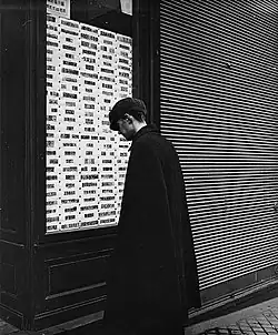 Photographié par Emil Mayer (de), homme observant des timbres-poste de collection proposés à la vente dans la vitrine d'un négociant spécialisé, à Vienne (Autriche), entre 1905 et 1914.
