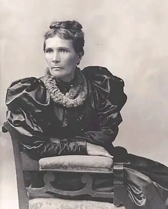 Portrait d'une femme pensive en robe noire satinée, assise.