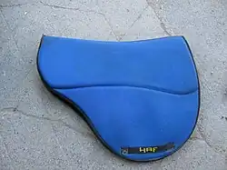 Tapis de selle bleu vif présentant une forme arrondie pour épouser les formes de la selle.