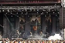 Un groupe de musique joue de jour sur une grande scène devant un public.