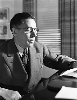 Un homme entre deux âges en costume cravate assis lit une lettre.