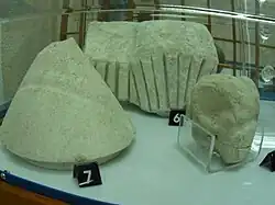 Trois pierres, devant la pierre est conique, une plus petite à droite a un motif émoussé, derrière, la troisième a des stries prononcées.