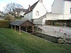 Photographie d'une bassin rectangulaire rempli d'eau et protégé par un toit, le tout appuyé à un haut mur.