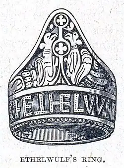 Dessin au trait d'une bague gravée de dessins et de lettres capitales.