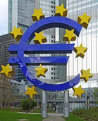 :Euro-Skulptur&nbsp;(en), monument représentant le symbole de l'euro entouré des étoiles du drapeau européen, devant l'Eurotower, ancien siège de la BCE, à Francfort-sur-le-Main.