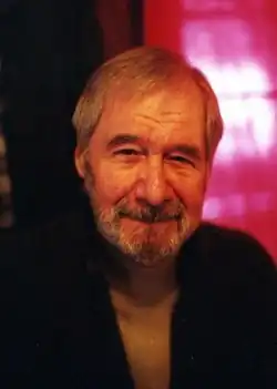 Photographie d'un homme qui regarde l'objectif de la caméra avec un sourire. Il se situe devant un fond rose.