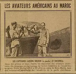 Article de presse montrant une photographie noir et blanc de deux hommes debout, devant la queue d'un avion. Deux chiens sont debouts sur l'empennage.