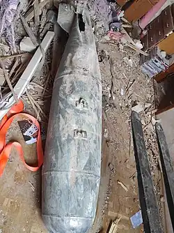 Photo des restes abîmés d'une bombe aérienne posés sur des débris.