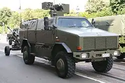 Un Dingo 2 de la Composante terre de l’armée belge avec une tourelle téléopérée tractant un obusier LG1 Mark II de calibre 105&nbsp;mm le 21 juillet 2016.