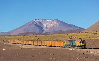 Un train, probablement chargé de minerai d'argent, de la mine de San Cristóbal au port d'Antofagasta. À l'arrière-plan, le volcan Ascotan&nbsp;(en). Juillet 2013.