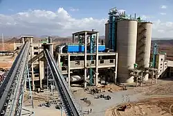 vue d'une usine avec deux convoyeurs au premier plan, un bâtiment de type industriel et quatre silos à leur droite