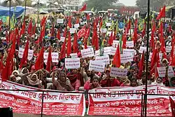 Foule d'Indiens et surtout d'Indiennes arborant des banderoles revendicatives et brandissant des drapeaux rouges ou jaunes et verts